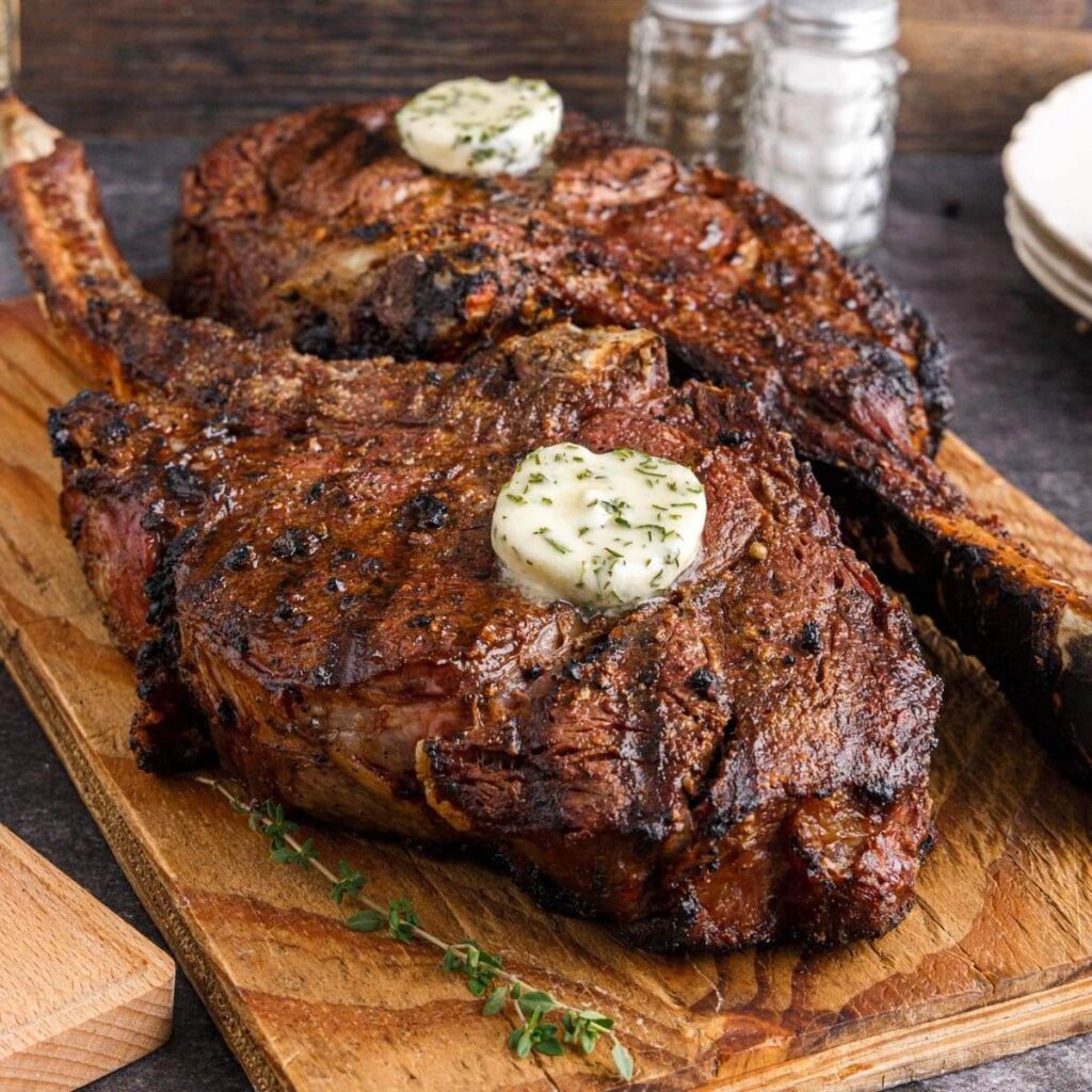Tomahawk ribeye steak cooking over open flames on a charcoal grill, with visible grill marks and sizzling fat.