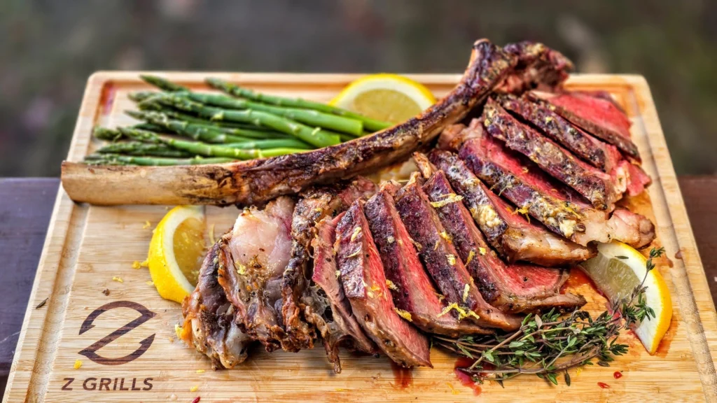 Sliced tomahawk ribeye steak served on a wooden cutting board with grilled asparagus, lemon wedges, fresh thyme, and a long rib bone.