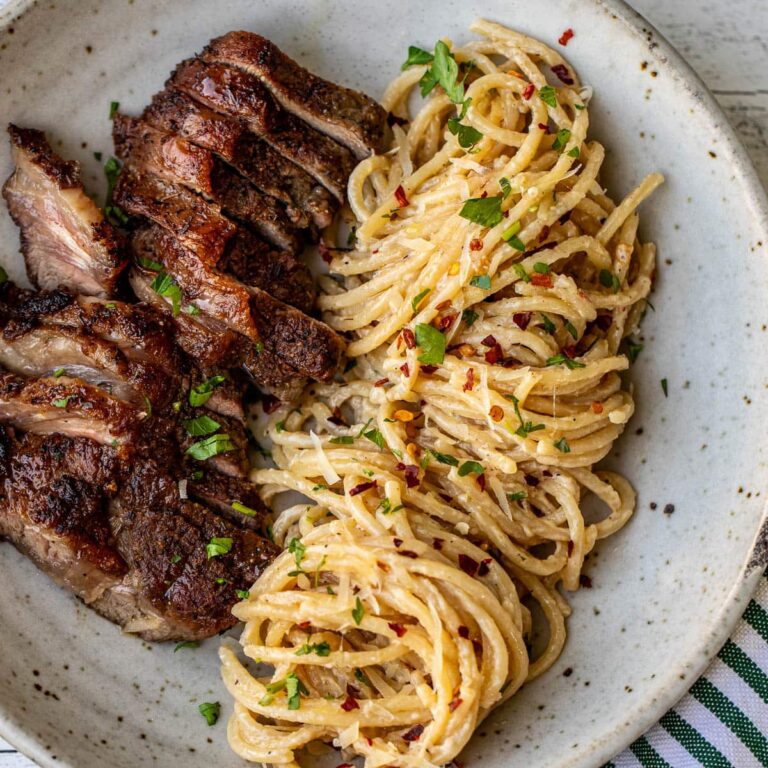 Creamy garlic parmesan pasta with sliced grilled steak on a ceramic plate