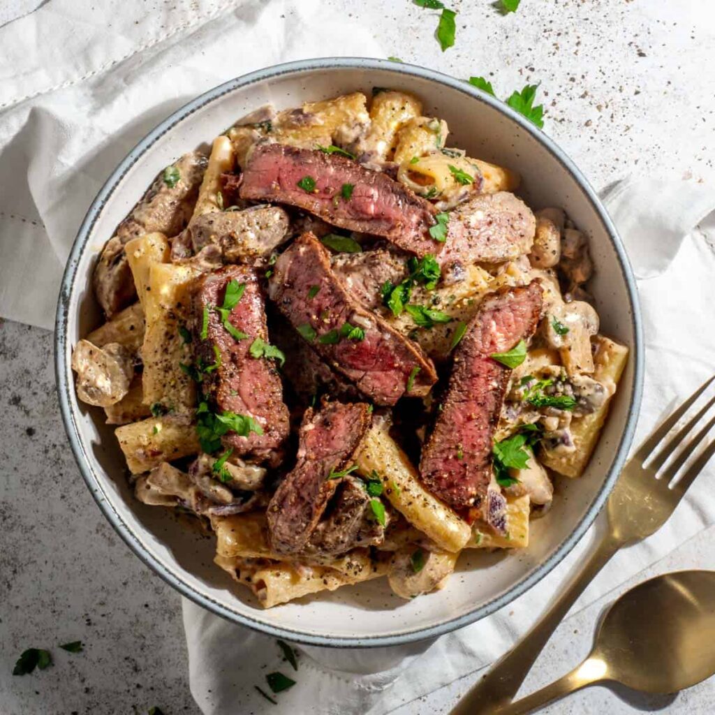 Sliced steak with creamy spaghetti topped with herbs and red pepper flakes
